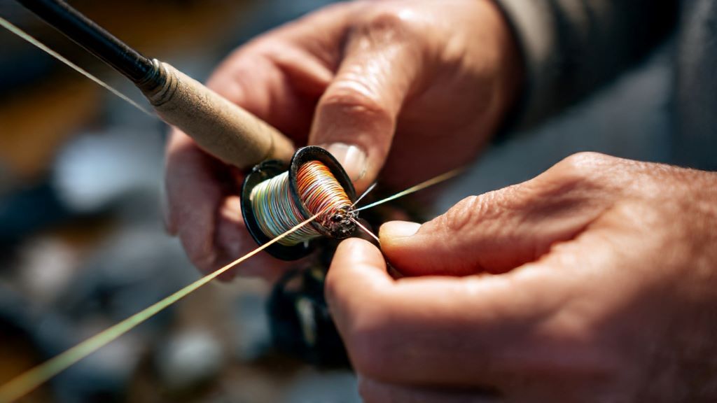 Angler repairing loose fishing rod guide with epoxy and thread wrap