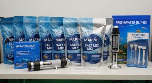 Various brands of marine salt mix bags displayed next to a refractometer and a freshwater testing kit on an aquarium shelf