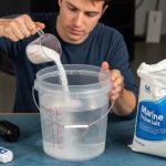 A beginner measuring marine salt into a bucket of purified water to prepare for a home saltwater aquarium setup