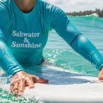 Surfer wearing a rash guard paddling on a surfboard