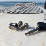 Close-up of stainless steel surfboard fin screws and a fin key laid out on a surfboard deck
