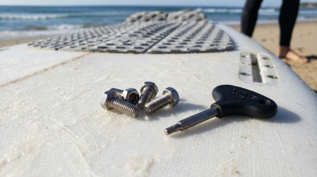 Close-up of stainless steel surfboard fin screws and a fin key laid out on a surfboard deck