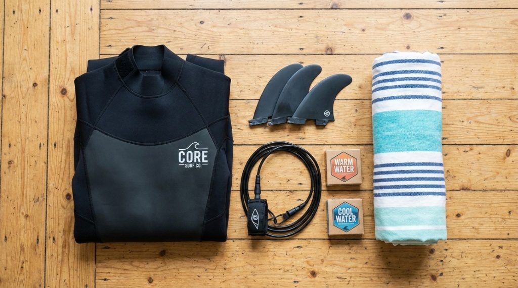 A top-down flat lay of an affordable wetsuit, surfboard fins, and surf wax.