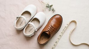 Childrens elegant white and brown wedding shoes next to a soft measuring tape.