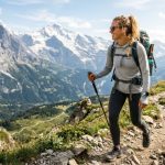 Athletic woman hiking up a sunny mountain trail wearing a protective grey sun hoodie.