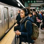 Commuter wearing durable wireless headphones on a busy subway platform.