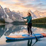 Person paddleboarding on a calm lake during sunrise.